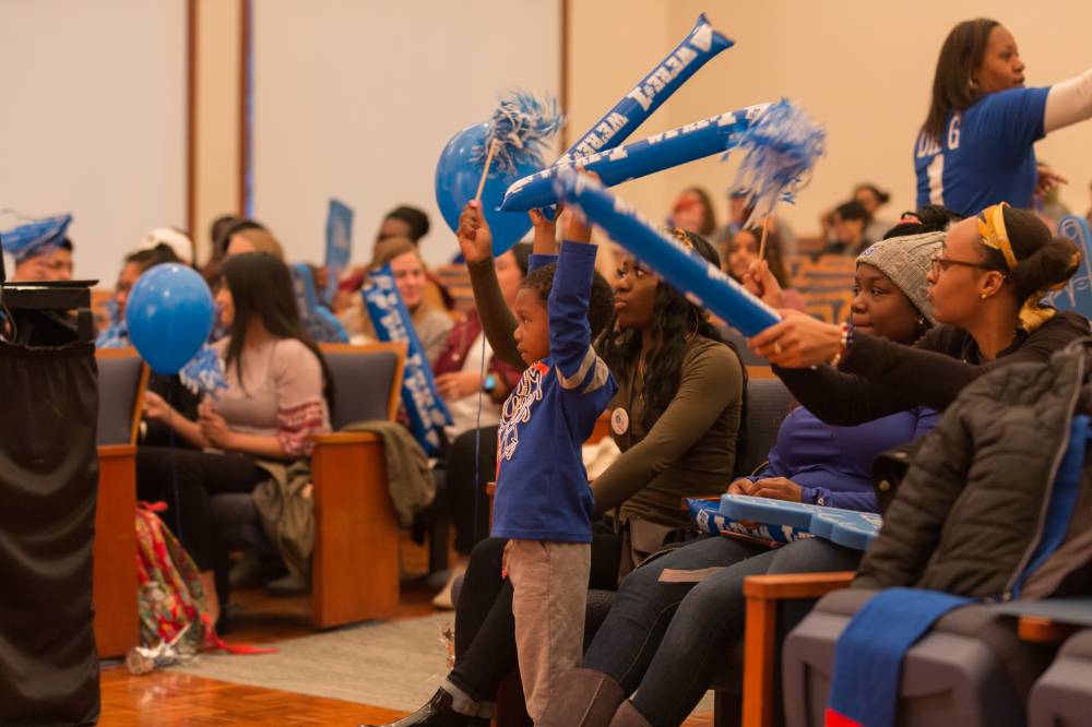 Image of people in audience. Young child showing excitement holding GVSU noisemakers